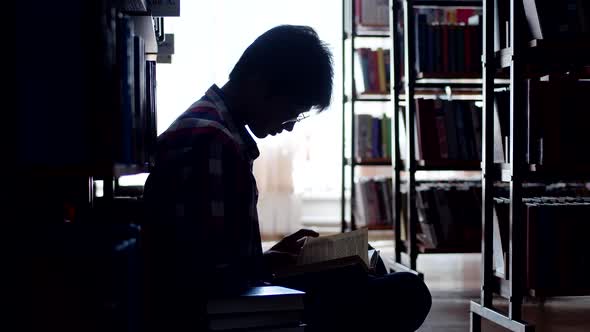 Young man is sitting on the floor in the library. silhouette of an asian man reading a book