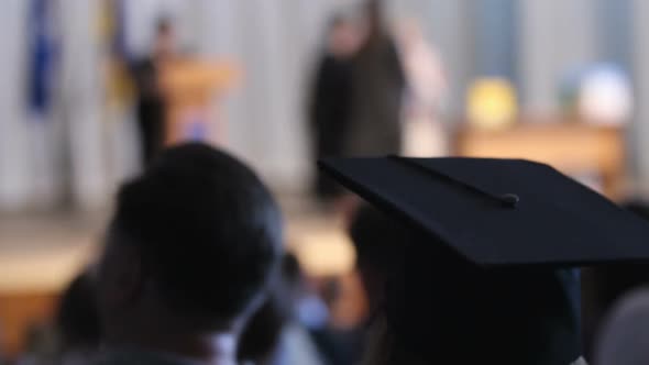 Girl Wearing Mortarboard Looking at Stage and Listening Rector's Congratulations