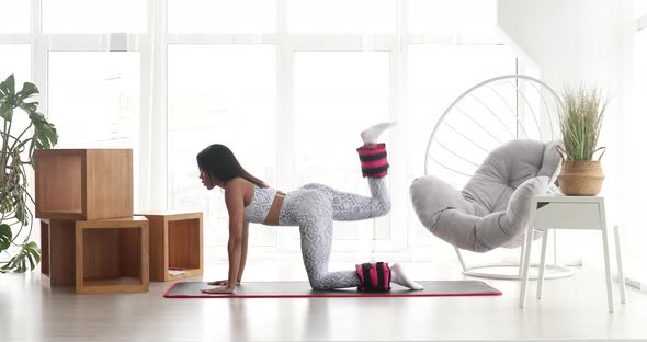 Pretty fitness black woman in sportswear practicing donkey kick exercise with ankle weight.