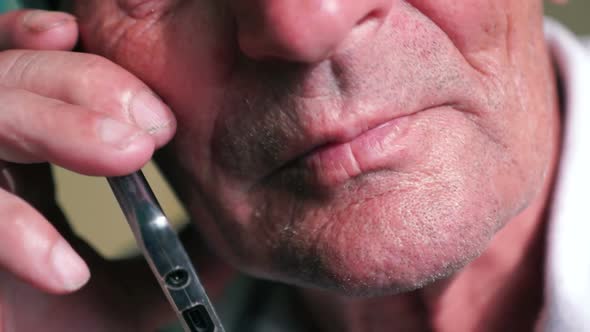 Close-up face of a Caucasian elderly man talking on the phone on a serious topic. Parts of the face