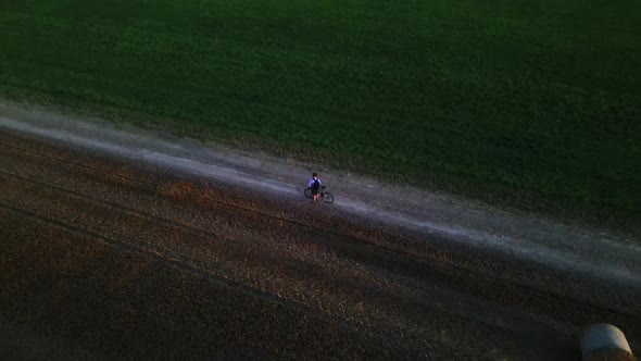 A cyclist stands with a bicycle on a country road between two fields.