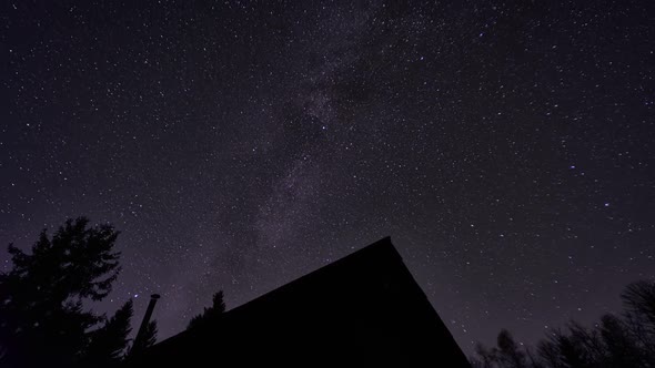 Night sky with the Milky Way. Silhouette of a wooden cottage among the trees.