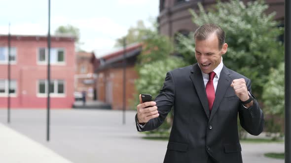 Businessman Celebrating Successful Results on Smartphone