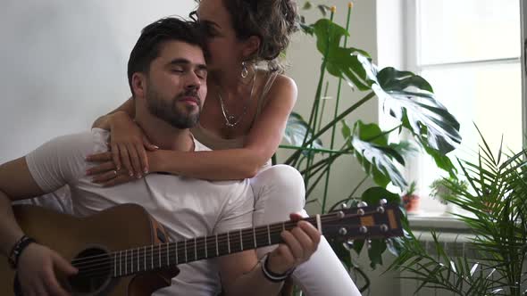 Loving Young Couple with Guitar Sitting on Sofa in Modern Apartment Spbd