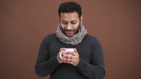 Indian Man in Scarf Warming Hands with Cup of Hot Tea Smelling Aromatic Drink Smiling at Camera