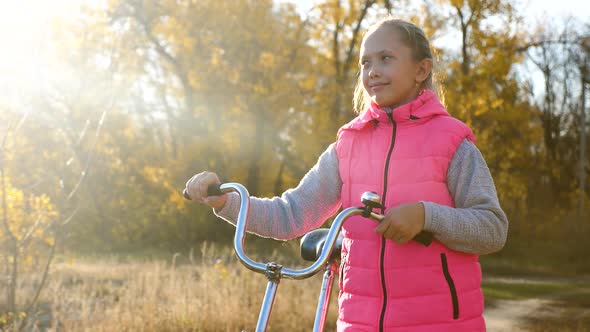 Child Travels with a Bicycle in the Park. Young Girl Walks. A Young Girl Walks Along the Road