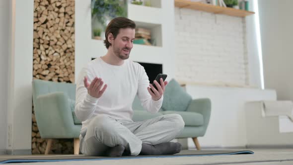 Young Man Talking on Video Call on Smartphone While Sitting on Yoga Mat