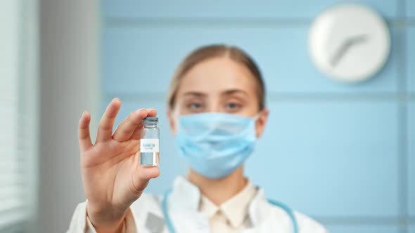 Serious lady doctor holds vaccine against covid in transparent vial standing in hospital