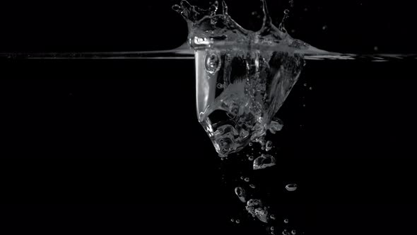 Ice cube dropped into water against black background. Slow Motion.