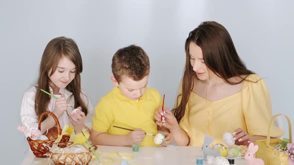 Mother Colouring Easter Eggs with Her Kids in White Room