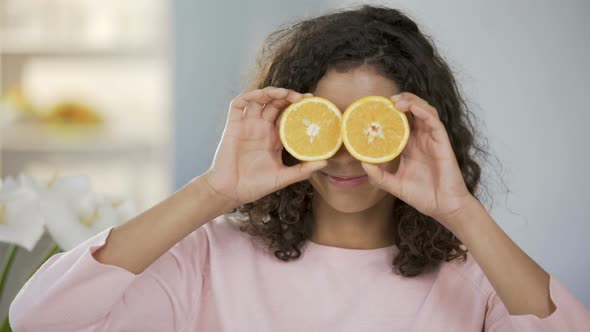 Mixed Race Girl Smiling at Camera, Holding Halves of Oranges Before Eyes, Health