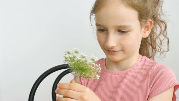 Little Girl is Sitting at Home with Flowers in Hands During Summer Time and Sneezing