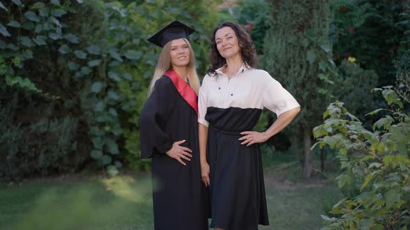 Happy Proud Mature Woman Posing with Graduate Young Daughter Outdoors on Summer Spring Day