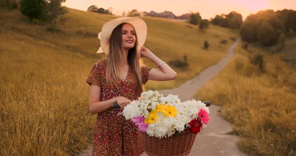 Porter Girl Walking on Camera in a Dress with Flowers in a Basket and a Bike in the Field