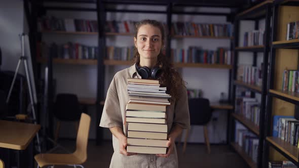 Smiling Student Holding a Lot of Books in the Library Preparing for Exams