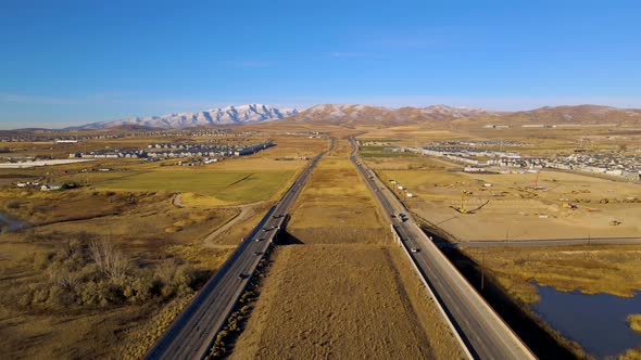 Flying above separated highway with light traffic in autumn with snowy mountains in the background