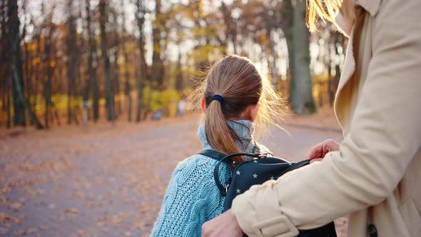 Young Mom Putting Plastic Container Into Backpack of Little Daughter Zipping It