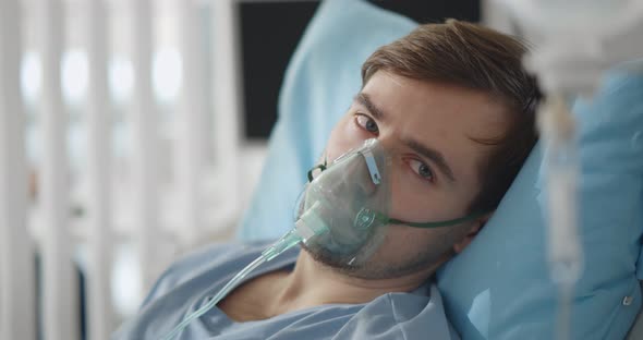 Young Attractive Man with Oxygen Mask Looking Sad and Worried Lying at Hospital Bed