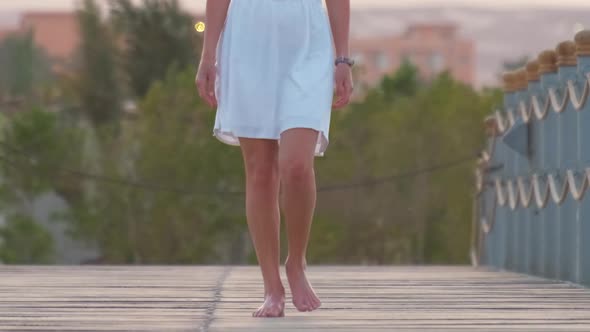 Closeup of Young Woman in White Dress Walking on Long Pier in the Evening