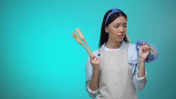 Incompetent Housewife in Apron Holding Kitchenware and Shrugging Shoulders