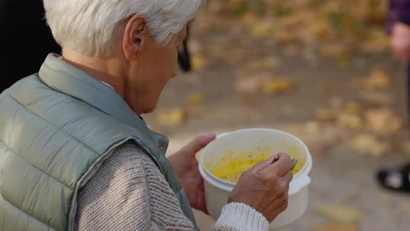 Gray Haired Old Woman Eating Charity Meal While Sitting on the Bench in the Park