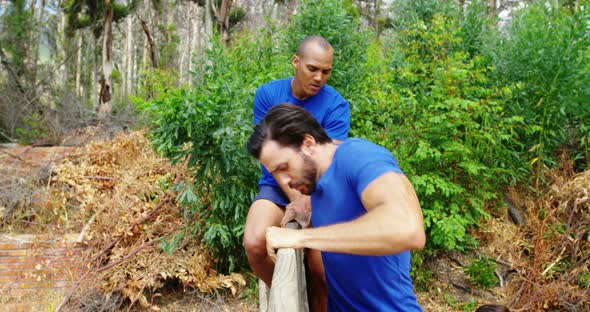 Male trainer assisting fit man to climb over wooden wall during obstacle course 4k