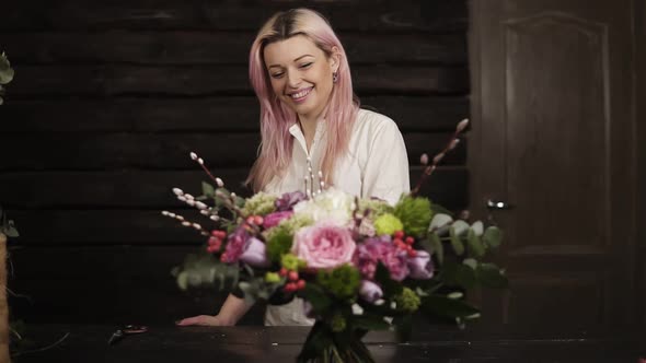 A Beautiful Girl with Pink Hair Smiles Admires a Stunning Bouquet of Flowers Lying on the Surface