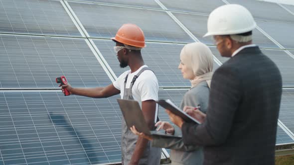 Muslim Woman with Laptop and Indian Man with Clipboard Standing on Solar Farm