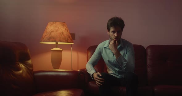 Pensive man sitting on the red sofa at home