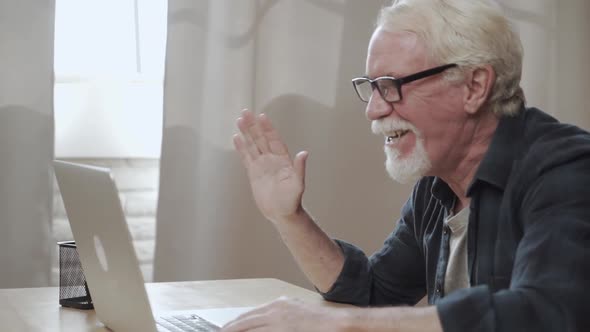 Handsome Smiling Older Man with Mustache and Beard Is Using a Laptop Computer for Online Video Call