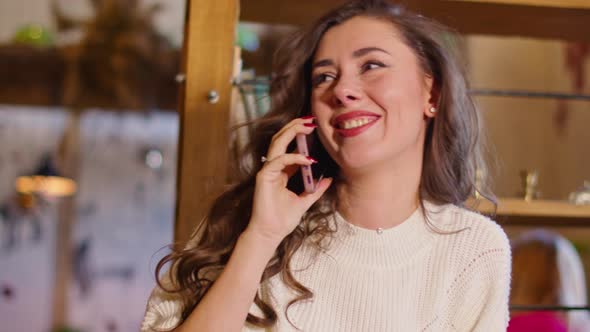 Happy Young Woman Speaks on the Phone in a Cafe Touches a Book with Her Hand