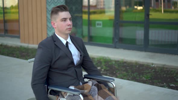 Young Businessman in a Suit in a Wheelchair. A Serious Man Rides in a Wheelchair and Looks at His