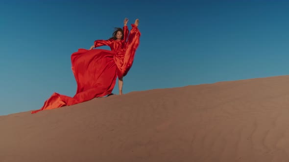 An Asian woman in a red dress dancing on sand dunes