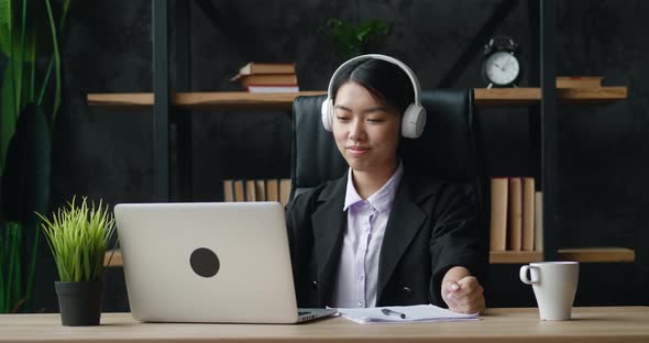 Happy Asian Businesswoman is Satisfied with the Work Done at the Laptop Computer Puts on Headphones