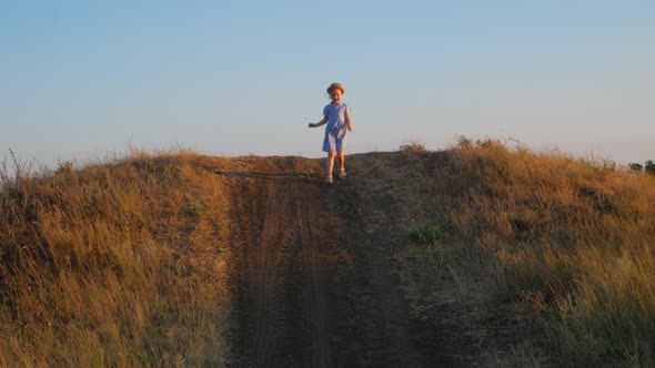 Adorable little girl in blue summer dress running down the hill and laughing. Happy child walking