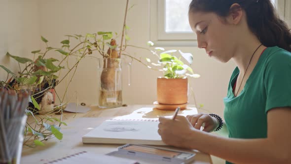 Teenage artist sitting drawing in a sketchbook in her room