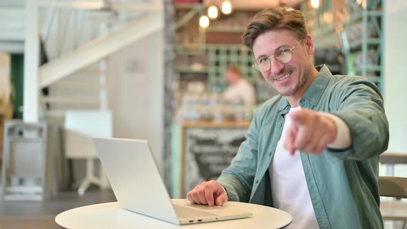 Middle Aged Man with Laptop Pointing at the Camera in Cafe 