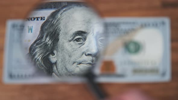 One Hundred Dollars Look Under Magnifying Glass on Wooden Table