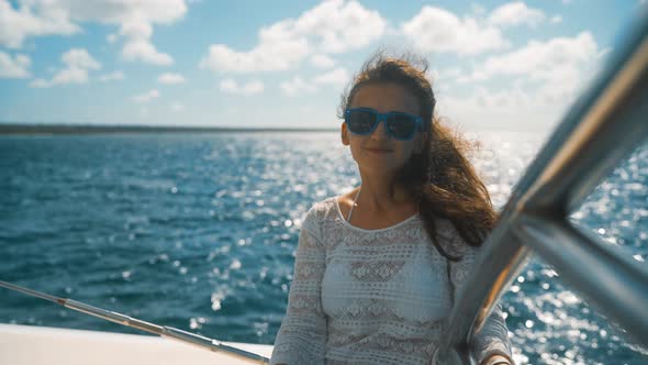 Girl in Sunglasses Sitting on the Edge of the Yacht Among the Sea