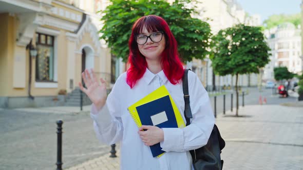 Positive Teenage Female Student Looking at Camera Waving Hand Outdoor
