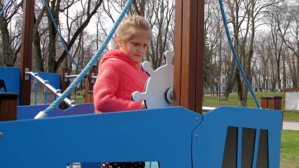 Young Schoolgirl Plays with Artificial Ship Wheel in Park