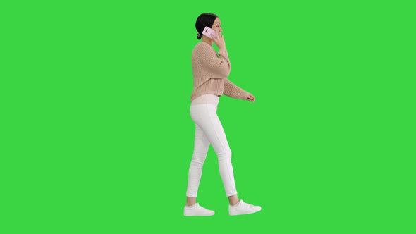 Smiling Young Woman Talking on the Phone While Walking on a Green Screen, Chroma Key.