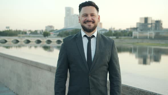 Portrait of Joyful Middleaged Businessman in Suit Standing Outdoors in City Embankment