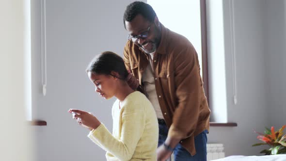 Smiling father collecting hair of daughter looking at phone