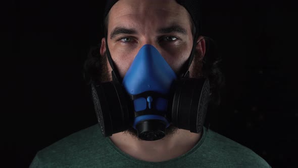 Close up footage of man wearing blue respirator over dark background