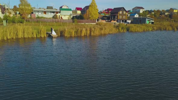 Newlywed Couple Hugs on Pier of Large Calm River Aerial View