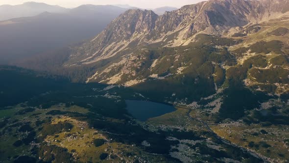Wide aerial drone slowly dropping capturing a lake and valley below a mountain range.