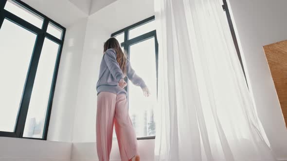 A Young Woman in Pastel Clothes Dances in Front of a Window