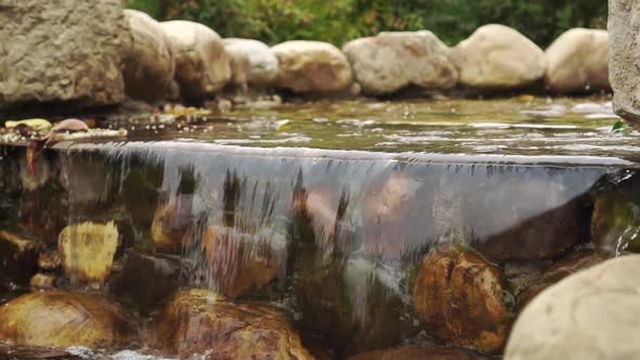 Falling water over brown mossy stones of a decorative waterfall.