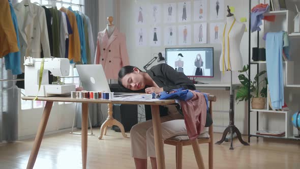 Female Designer In Business Suit Working On A Laptop, Yawning, And Sleeping While Designing Clothes